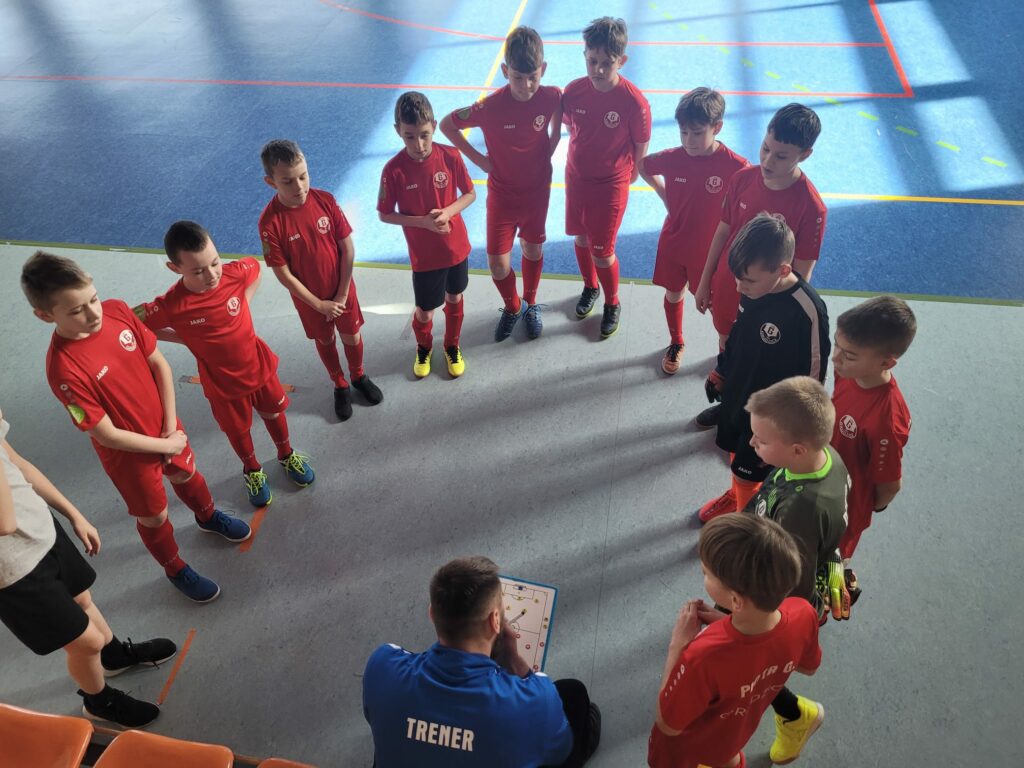 Zawodnicy Akademii słuchający wskazówek trenera w przerwie meczu